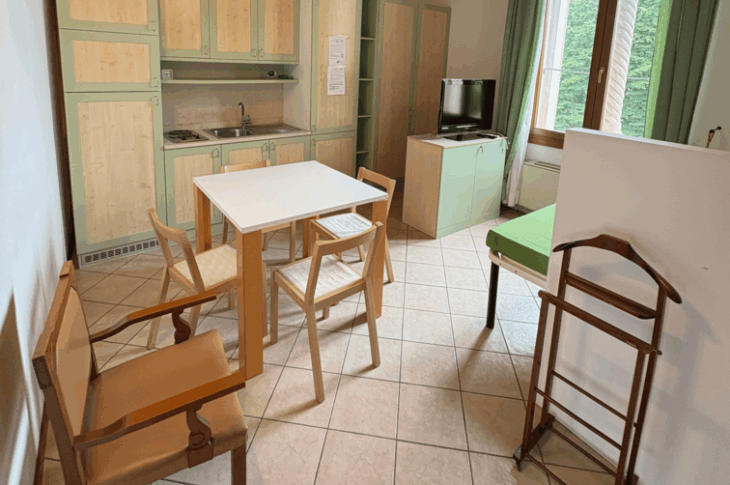 Letto, tavolo, cucina e finestra su giardino, con travi a vista e arredi semplici