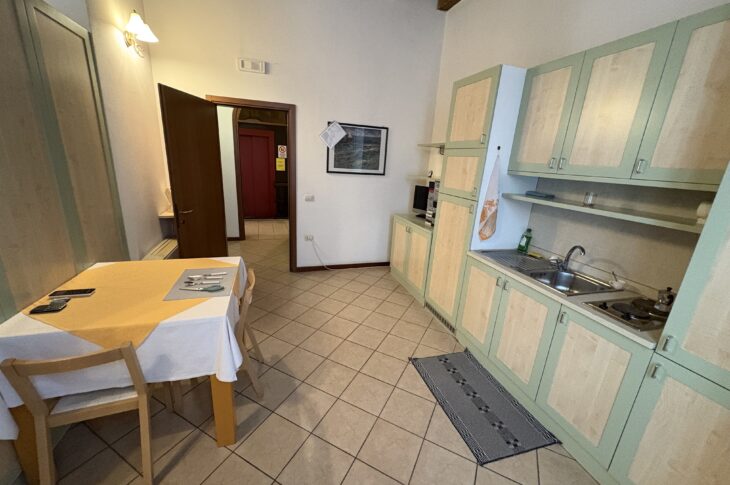 Cucina compatta con tavolo apparecchiato, mobili chiari e travi in legno sul soffitto