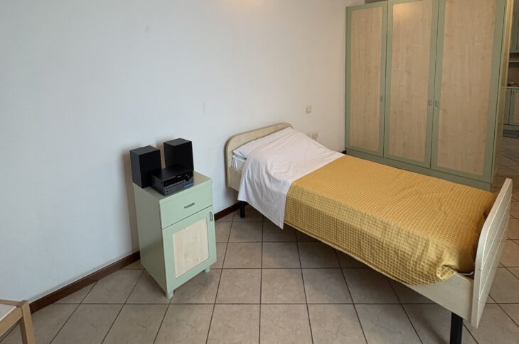 Letto singolo con stereo sul comodino, armadio verde e soffitto con travi a vista