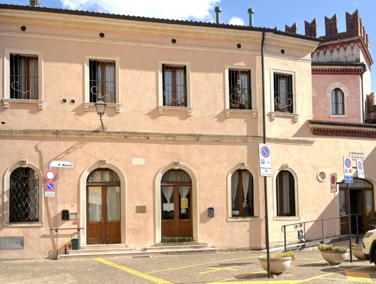 Edificio rosa con porte in legno, targhe e segnali stradali in una via tranquilla Edificio rosa con porte in legno, targhe e segnali stradali in una via tranquilla
