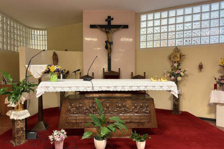 Crocifisso, fiori e oggetti dorati su un altare con tovaglia bianca in una chiesa