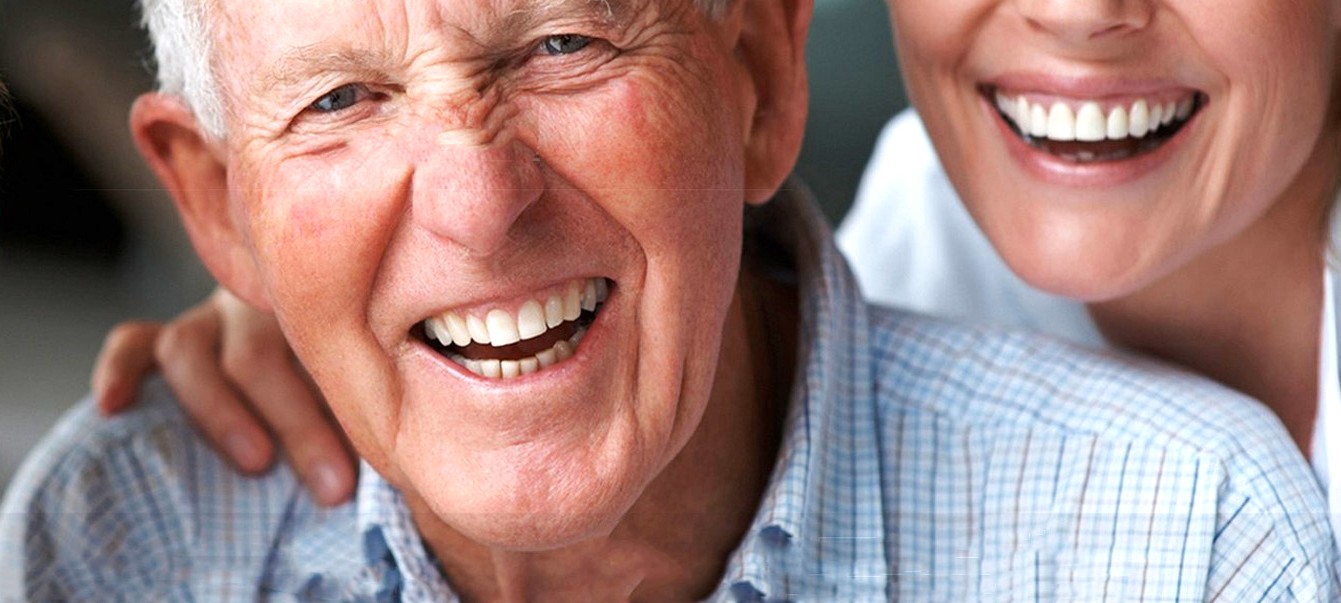Primo piano di due persone che sorridono, una mano sulla spalla dell’anziano