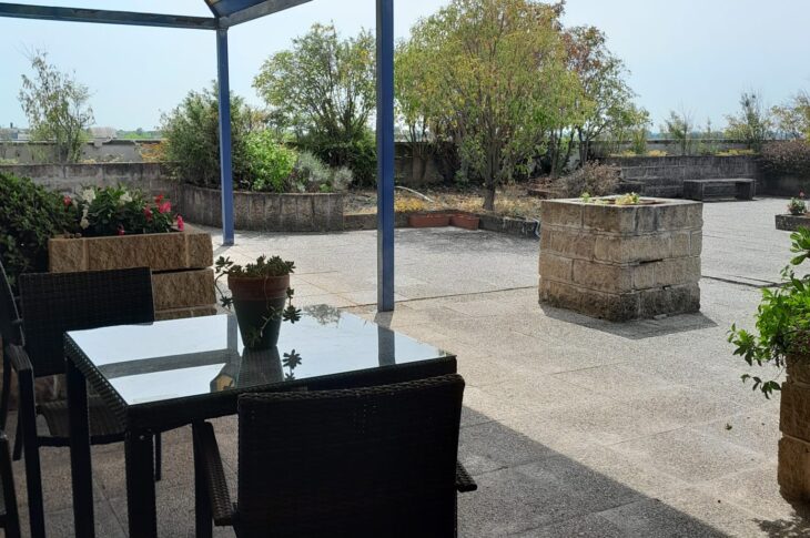Porticato con tavolini e sedie sul terrazzo con giardino.
